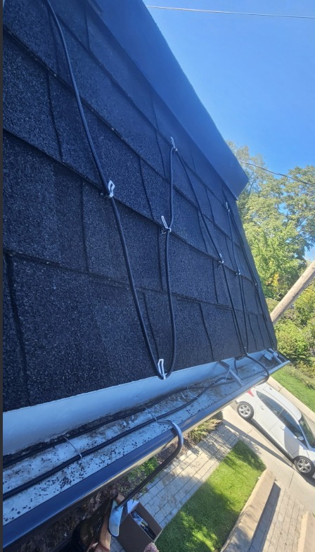De-icing heating cable clipped in a zigzag pattern on a dark shingle roof edge and run into the eavestrough