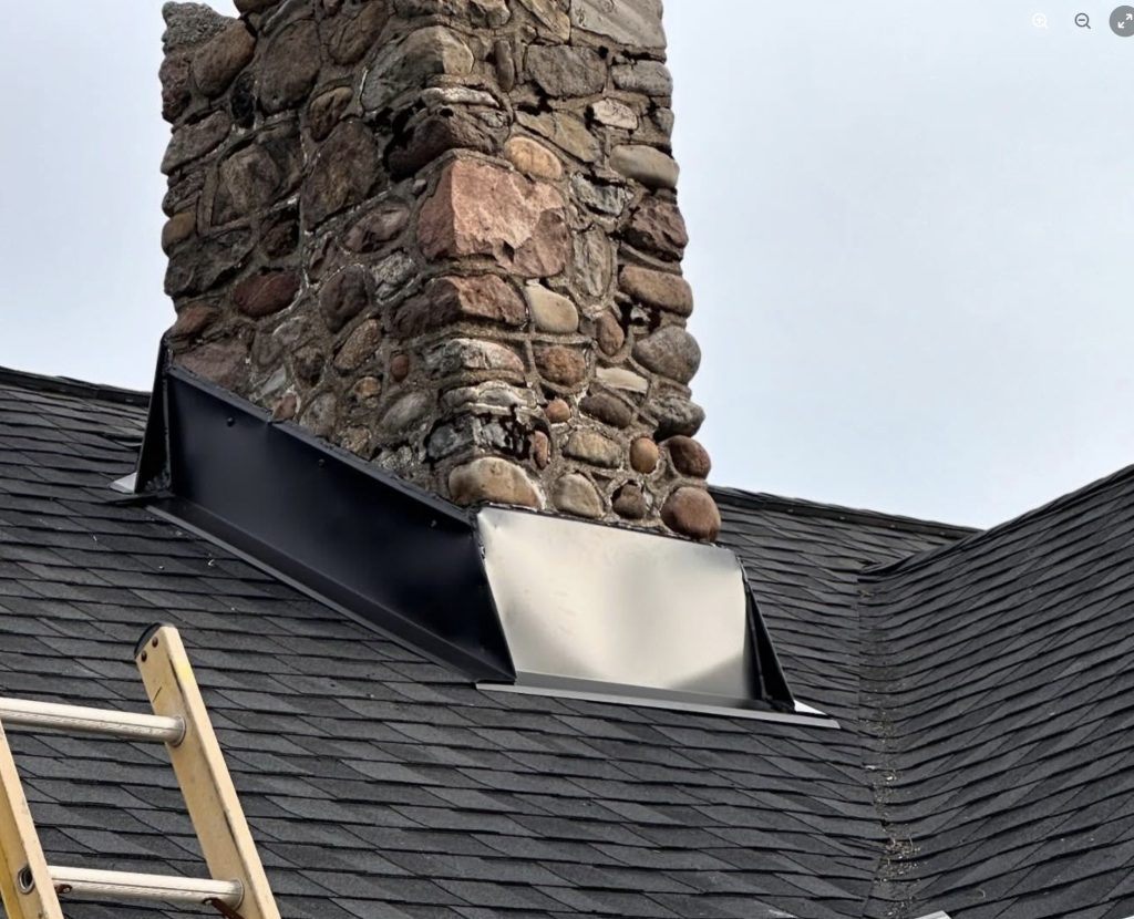 Stone chimney with new metal flashing on a dark shingle roof