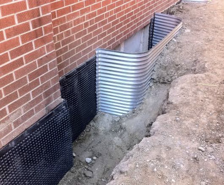 Basement window well installed against a brick wall with dimpled foundation membrane