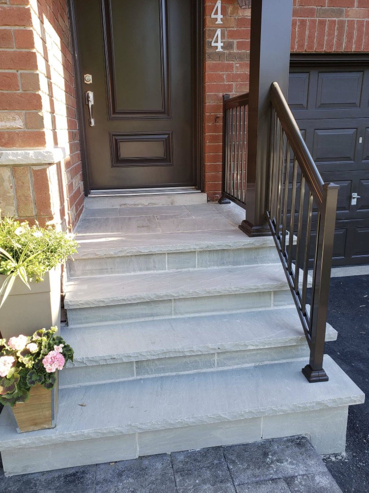 Rebuilt front entrance with grey flagstone steps and a dark aluminum railing beside a brick wall and front door