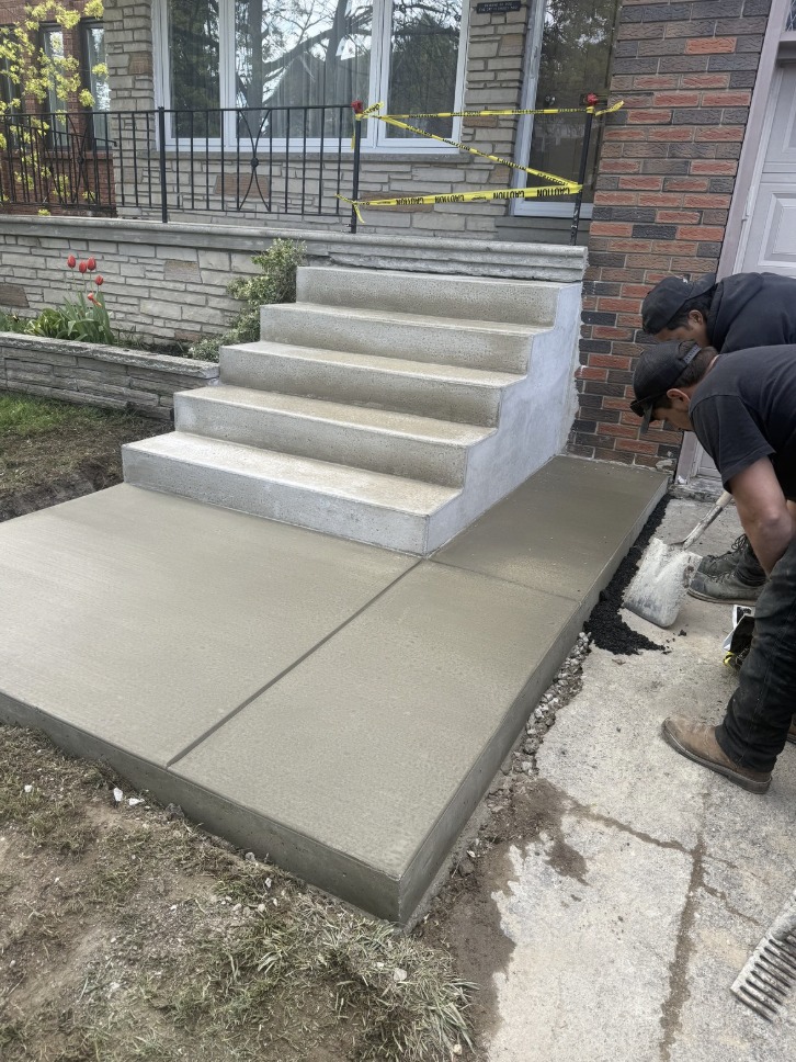 Newly poured concrete front steps and landing with our crew finishing the job beside a stone planter wall