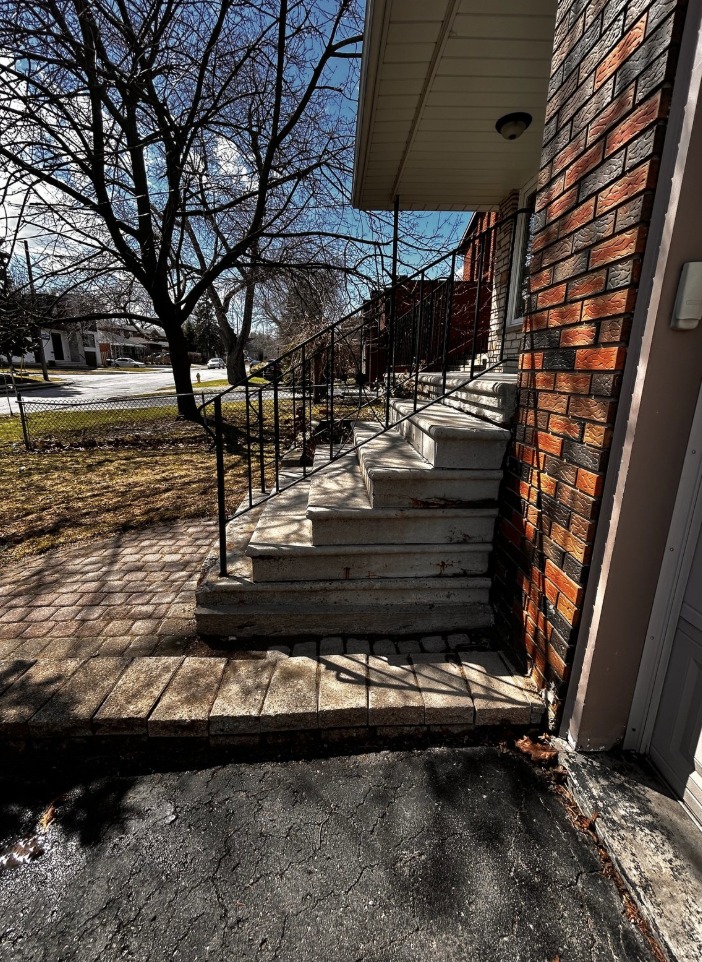 Worn concrete front steps with a rusting iron railing and interlock border, in need of repair